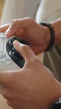 Vertical video: Pressing gamepad button, hands moving stick on couch gaming with watch, bracelet