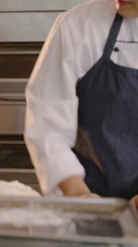 Vertical video: Placing dough on scale, baker in coat weighing, shaping rolls at bakery for baking