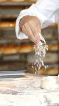 Vertical video: Arm reaching left, dusting flour, baker shaping dough on bench coat bowl for baking