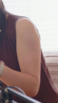 Vertical video: Woman in sleeveless top adjusting mic boom at window for recording, holding card