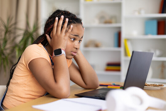 Black teenage girl looking worried while studying on laptop at home. Concept of academic stress, online learning difficulties, concentration problems, and educational pressure