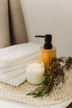 Minimalist still life of luxury spa essentials. White cotton towels with visible textured, bottle with oil and soy wax candle.
