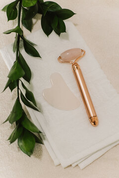 Facial rose quartz stone massage roller and gua sha massager on a white towel background.
