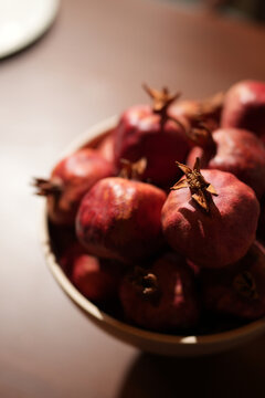 Fresh ripe pomegranates in a modern white ceramic bowl on a wooden table, cozy stylish kitchen blurred interior background
