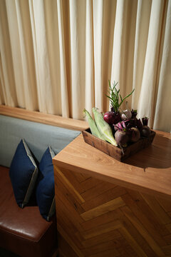 Fresh organic vegetables including corn, beetroot, and red onions with garlic in a rustic wooden tray on a table. Cozy kitchen interior