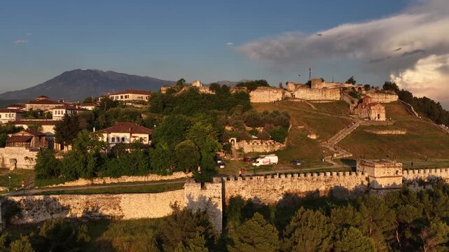 Aerial view of the historic Berat Castle, featuring ancient stone walls, traditional houses, and the Holy Trinity Church, set against rolling hills in Berat, Berat County, Albania.