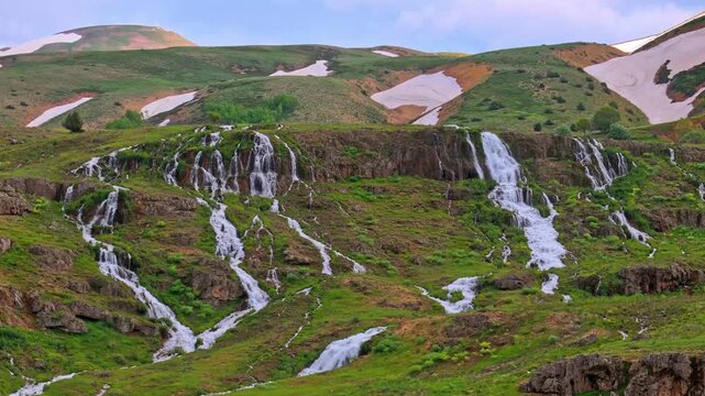 Scenic drone shot of multi-tiered Konarli Waterfall with snow capped hills in Tercan, Erzincan Turkey