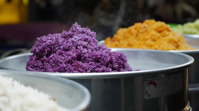 Metal containers filled with colorful steamed rice displayed at a market food counter forming a bright traditional food presentation in a public selling space. Traditional market.