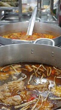 Vertical view shows Bun Mang Vit soup boiling in a large metal pot at a busy market stall counter during active cooking in an open public trading area. Street kitchen.