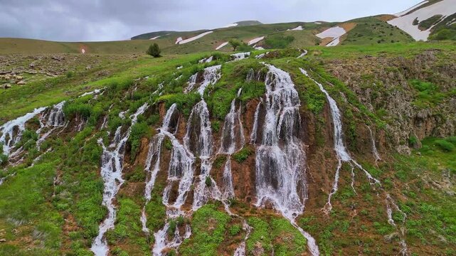 Scenic view of a multi-tiered waterfall flowing through green highlands with melting snow on mountains