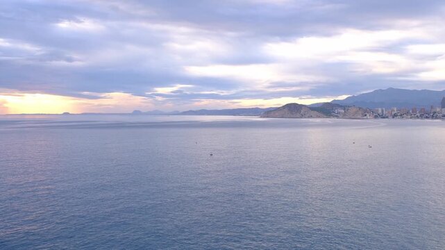Cala Tio Ximo coastline captured in December evening light. Tranquil winter sea, soft sunset glow, peaceful view of small island near Benidorm. Quiet natural beauty, no people, only sea and sky.
