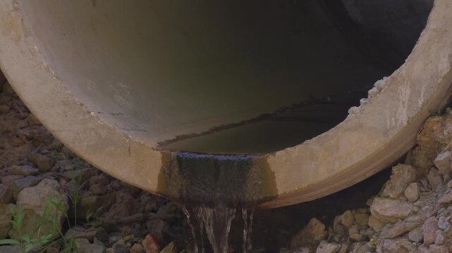 Water flows from a concrete pipe in a rural area at midday under bright sunlight