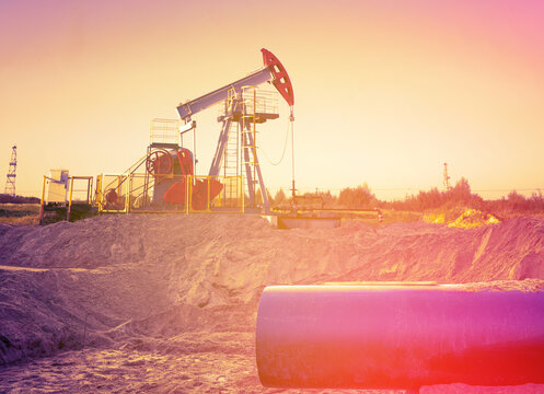 Oil drilling site on sunset with pump jack and pipeline in background. Extraction of petroleum. Fossil crude. Crude pump jack working on oil field on bright sky. Pumpjack, Oil drill, pipe, pipeline.