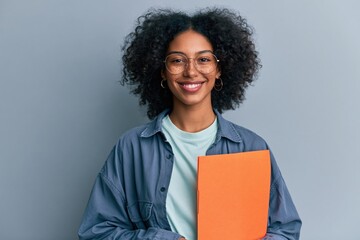 Obraz premium Young student smiling holding an orange folder in a casual jacket for education website banner and portrait background