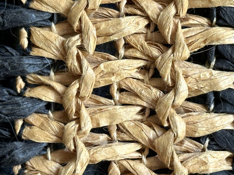 Close up of woven natural raffia and dark fibers creating a textured pattern feeling rustic and organic