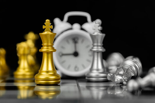 Golden chess king standing before defeated silver pieces and alarm clock on chessboard representing strategy.