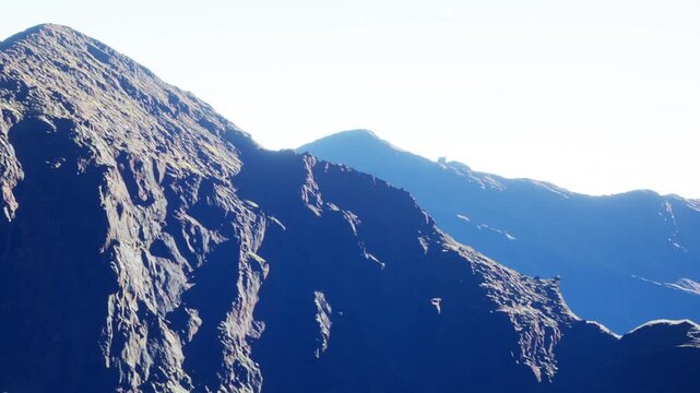 Mountains stretch across the horizon with rocky surfaces and varied textures. Bright sunlight highlights the peaks in the afternoon. Nature shows its power and beauty in this landscape.