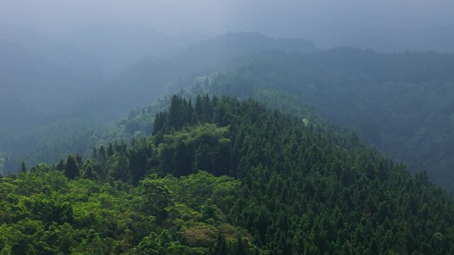 Aerial view of a lush green mountain ridge covered in dense forest under a misty sky in Sukabumi, West Java, Indonesia.