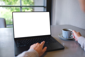 Fototapeta premium Mockup image of a woman working on laptop computer with blank white desktop screen while drinking coffee in cafe