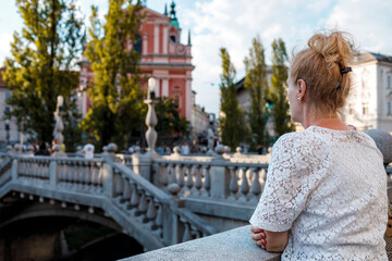 Fototapeta premium Woman stands on a bridge looking at buildings in the city during the day with people nearby
