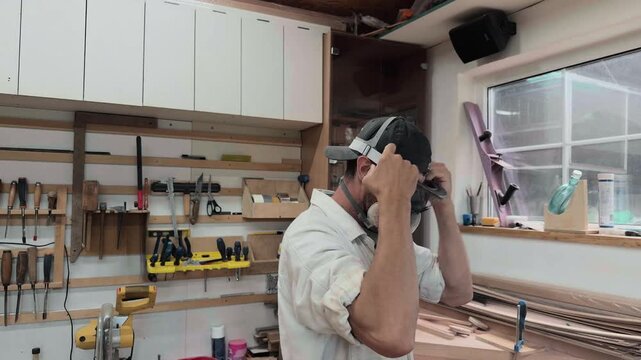 Dedicated cabinetmaker wearing respirator mask putting on protective safety goggles in bright woodworking shop pulling back to reveal authentic garage studio environment cinematic medium shot
