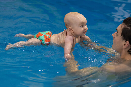 Smiling happy baby in the fun swim panties swimming with father in swimming pool. Swimming lessons.