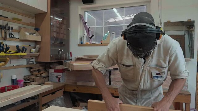 Focused artisan in full PPE ripping raw timber block on table saw facing camera intense eye level action close up in bright fabrication workshop authentic documentary b-roll