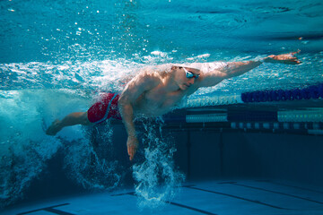 Male swimmer training underwater in pool lane. Concept of competitive swimming, athlete performance, freestyle technique, race preparation, and aquatic sports. © master1305
