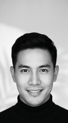 Fototapeta premium Portrait of a smiling young Asian man in a black turtleneck sweater in a studio setting