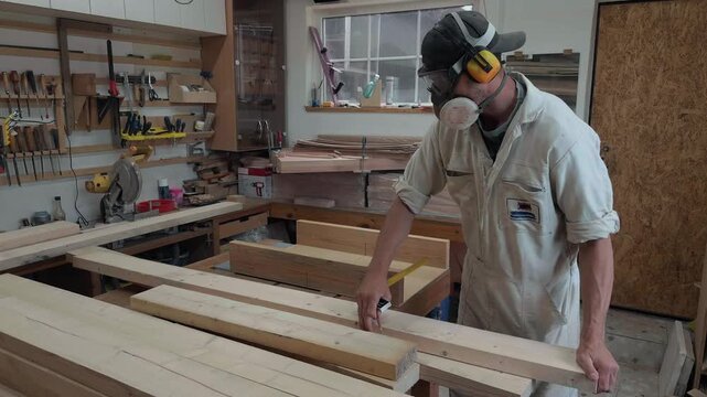 Meticulous anonymous artisan marking raw timber plank with pencil and yellow try square on lumber stack in rustic garage workshop during daytime authentic tracking close up pushing in on hand