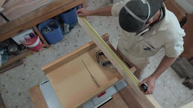 Meticulous local joiner in white uniform drafting precise cut lines on raw hardwood plank using a traditional metr folding tool and pencil in bright fabrication shop technical authentic handheld shot