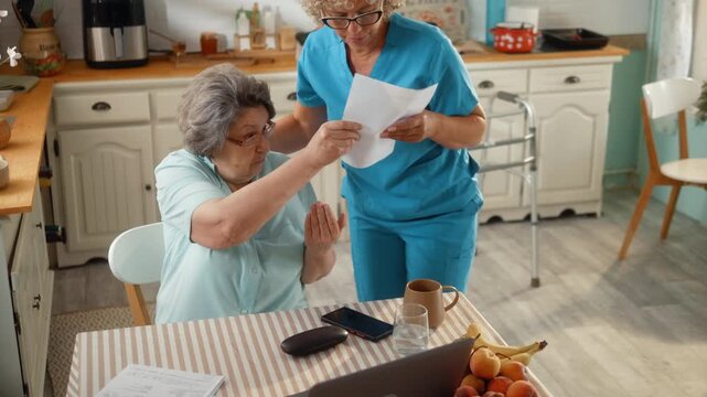 Senior woman and her caregiver review high household bills together, expressing concern about rising living costs and everyday financial challenges at home.
