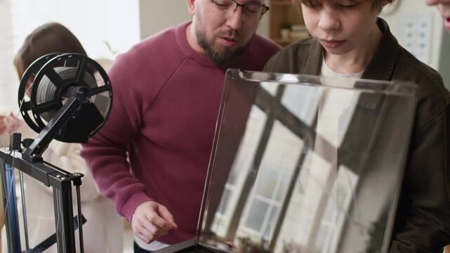 Close up tilt down shot of two teenage students enthusiastically observing 3D printing process together with their male teacher during class