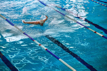 Naklejka premium Male swimmer practicing backstroke with water splash in pool. Concept of competitive swimming, sports training, aquatic fitness, and performance improvement.