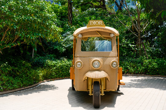 A unique wicker and wood Dior tuk-tuk sits among green foliage at Boutique Dior Gold House on Phloen Chit Road, Lumphini, Bangkok, Thailand, April 27, 2026