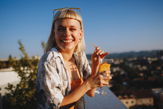 Happy woman toasting a cocktail on urban rooftop at sunset
