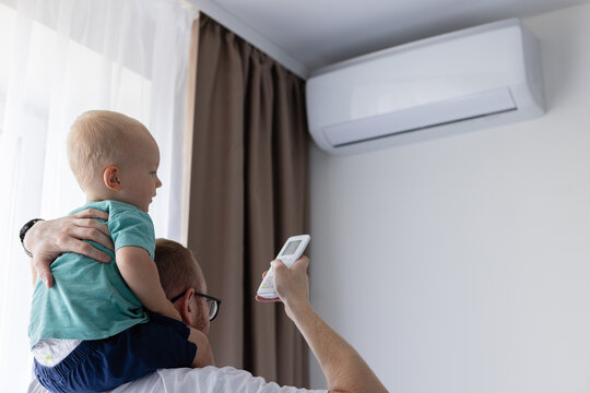 Father with little son on his shoulders turns on air conditioner using remote control.