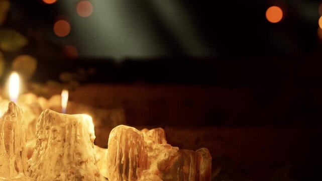 Several wax candles are lit in a dark area. The glow creates a warm atmosphere. Small groups of people can be seen around them, engaged in quiet conversation.