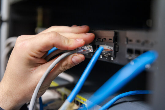 Close-up of a technician's hand plugging a grey ethernet network cable into a router or switch port.