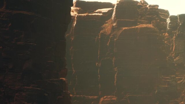 Rugged cliffs rise high against the clear sky, bathed in sunlight. The rocky formations create shadows and highlight the textures of the stones. This scene captures nature&rsquo;s raw landscape.