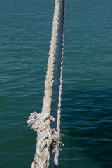 Fototapeta premium Close-up of a sunlit nautical rope with blurred blue sea water surface on background, summer travel concept.