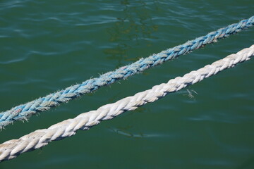 Fototapeta premium Close-up of a sunlit nautical rope with blurred blue sea water surface on background, summer travel concept.