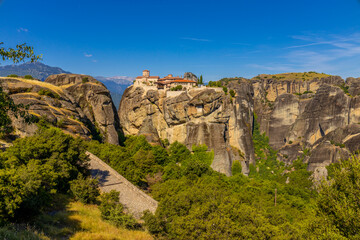 Fototapeta premium Meteora in Greece features towering sandstone rock pillars rising above valleys and forests, crowned by historic Orthodox monasteries. This UNESCO World Heritage Site offers breathtaking views