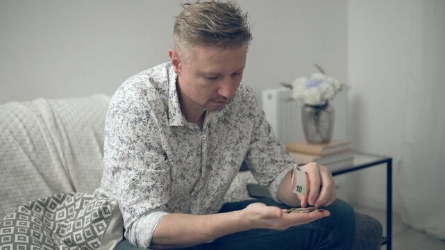 Young Man Counting Money Followed By Coins And Banknotes At Home
