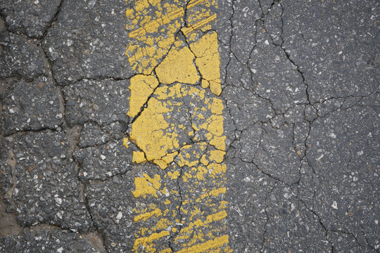 Cracked road with faded yellow line in urban area