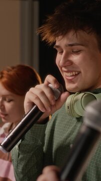 Vertical panning shot of multiethnic teenagers singing into microphones during rehearsal on stage. Clip for youth talent shows, music education programs, school extracurricular activities promotions
