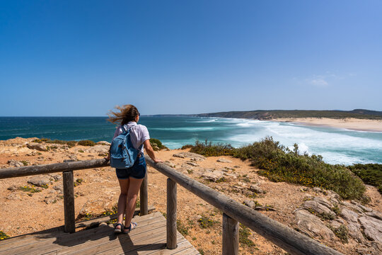 Visiting Algarve coast in Portugal. Beautiful middle-aged woman tourist standing  at Carrapateira viewpoint and enjoying vacations over ocean on summer day. Back view
