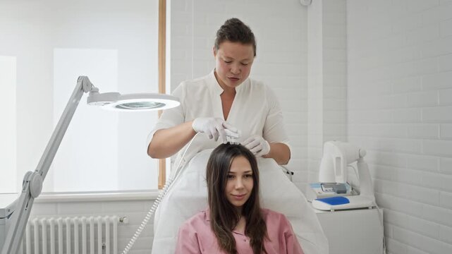 Caucasian female trichologist examining Caucasian female patients scalp, using diagnostic tool. Ideal for promoting hair loss treatments and dermatology clinic services