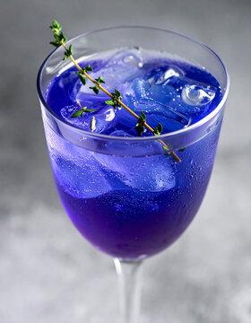 Butterfly pea flower cocktail with sparkling carbonation, fresh thyme floating on top, color-shifting blue purple drink, trendy bar presentation. Close-up.