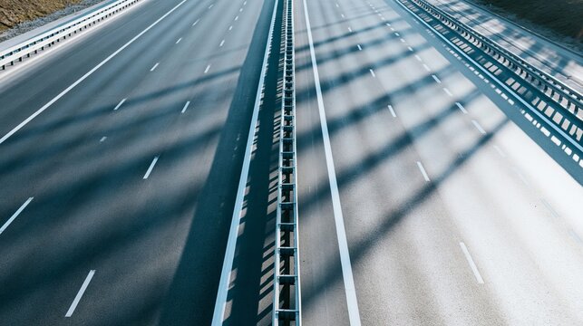 Empty highway lanes with white markings and safety barrier, long shadows falling across the road, creating geometric patterns
